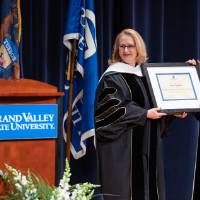 Recipient and President holding framed award while Provost speaks